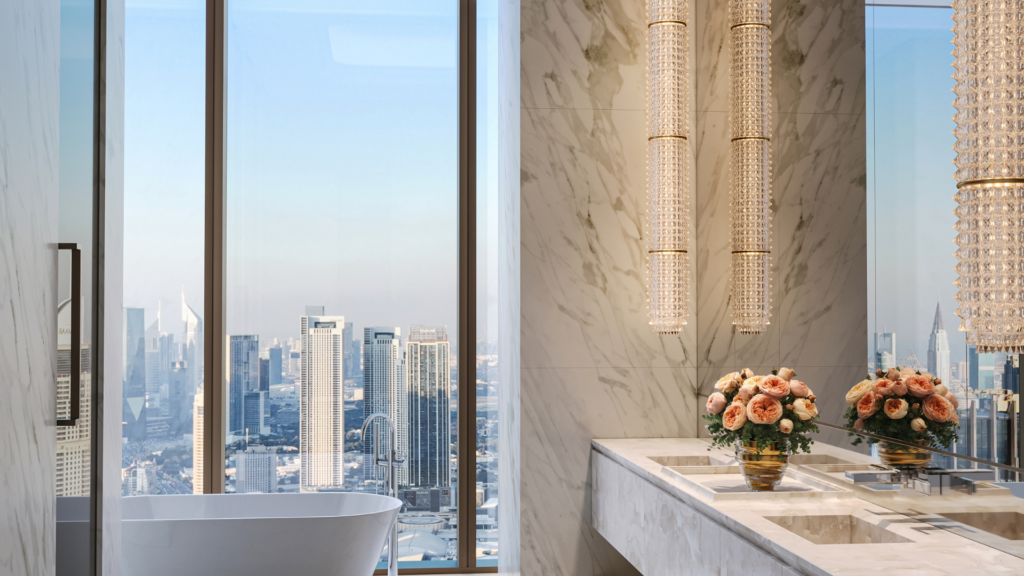 Il lussuoso bagno del Waldorf Astoria Business Bay Dubai è caratterizzato da pareti in marmo, vasca freestanding, finestre a tutta altezza con vista sulla città, due lavandini, eleganti lampadari e composizioni floreali rosa sul piano di lavoro.