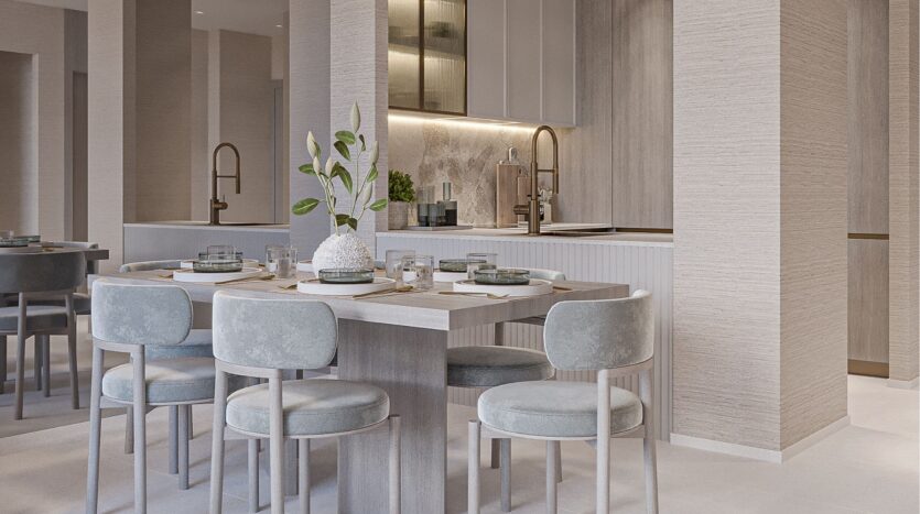 Salle à manger moderne avec une table en bois pour six personnes, des chaises coussinées bleu clair et un vase blanc avec des feuilles vertes. Profitez de la belle vie zimaya grâce à la cuisine aux tons beiges, avec ses étagères ouvertes et son éclairage sous l'armoire en arrière-plan.