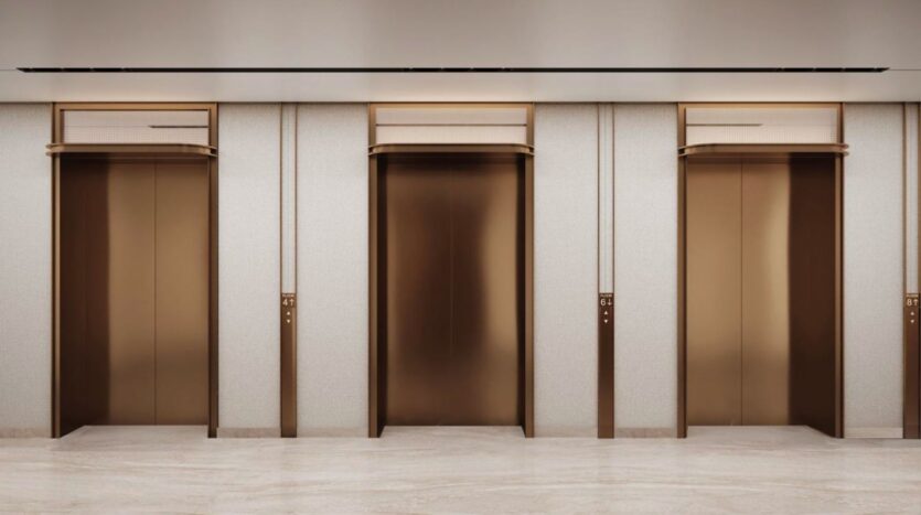 Three closed, gold-colored elevator doors are set into a light-colored wall with matching gold trim in Marquis One Arjan's modern lobby, featuring a sleek marble floor.
