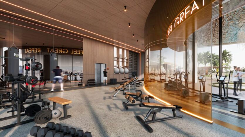 Modern gym at Marquis One Arjan with various workout equipment, benches, weights and treadmills. Large windows flood the space with natural light. Warm lighting and sleek design create a welcoming atmosphere for all fitness levels.