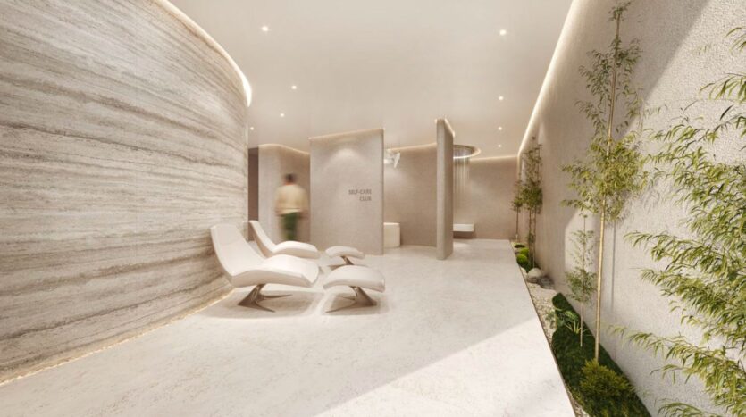 Minimalist spa lounge at Marquis One Arjan with modern white chairs, curved textured walls, indoor plants, soft lighting and a blurred silhouette passing in front of the "SELF CARE CLUB" wall. The space exudes a calm, serene atmosphere.