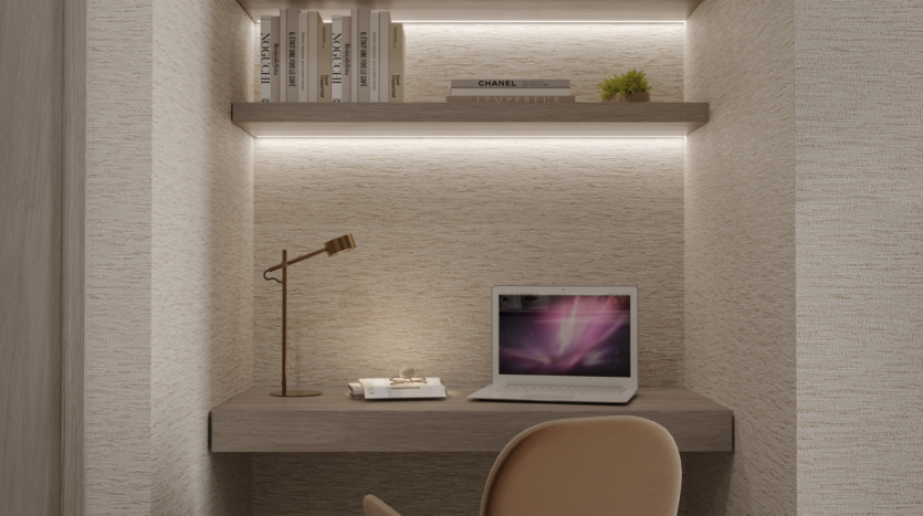 Una zona de oficina minimalista con un escritorio de madera, una silla beige, un portátil abierto, una lámpara de escritorio dorada, un cuaderno y dos estanterías con libros y una pequeña planta, todo ello iluminado por una suave luz integrada.