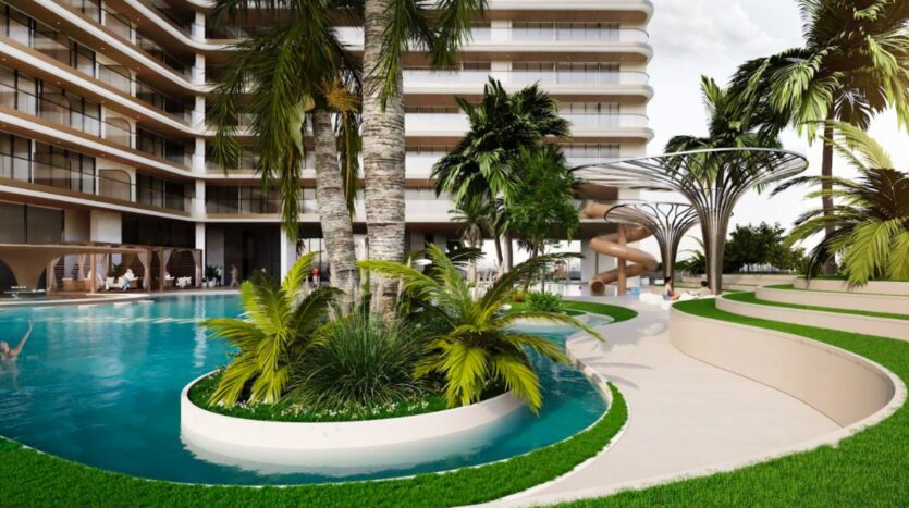 Marquis One Arjan is a modern complex featuring a curved pool with palm trees, lush landscaping and a spiral slide next to a multi-story building with balconies. Picturesque paths and green spaces surround the pool.
