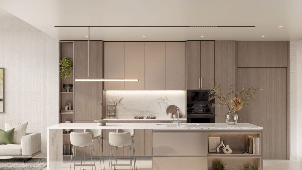 The modern kitchen in Riverton House by Ellington Properties features light wood cabinets, a marble backsplash, a built-in oven and a large island with two bar stools. Minimalist decor includes vases with dried flowers and neutral tones.