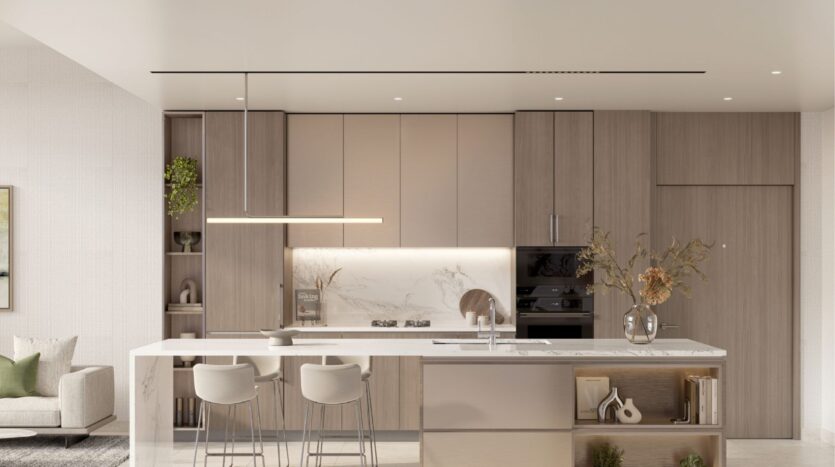 The modern kitchen in Riverton House by Ellington Properties features light wood cabinets, a marble backsplash, a built-in oven and a large island with two bar stools. Minimalist decor includes vases with dried flowers and neutral tones.