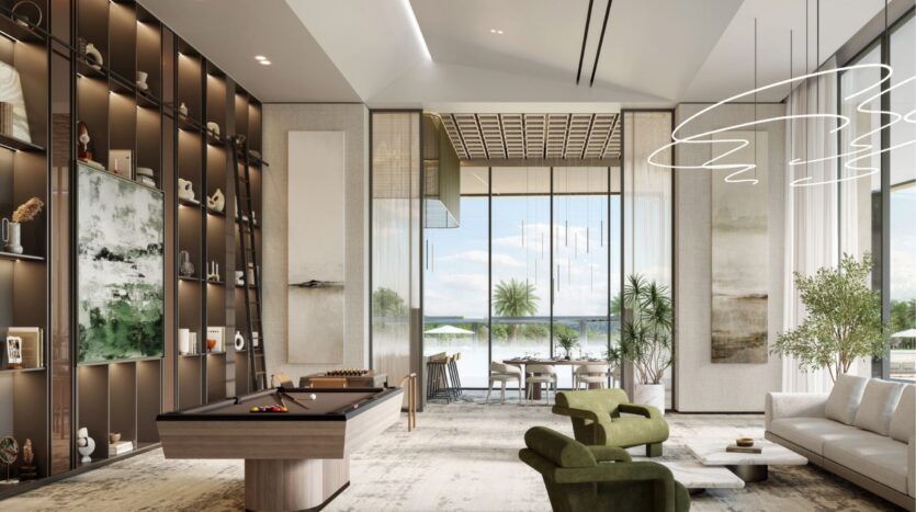 The modern, spacious living room at Riverton House by Ellington Properties features high ceilings, a pool table, green armchairs and shelves filled with artwork. Floor-to-ceiling windows overlook a lush patio with greenery and blue sky views.