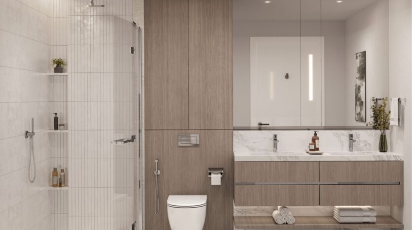 The modern bathroom at Riverton House by Ellington Properties features a glass shower, built-in shelving, wall-mounted toilet, large mirror, wooden cabinets, marble vanity, towel rolls, soap dispensers and a small vase with flowers.