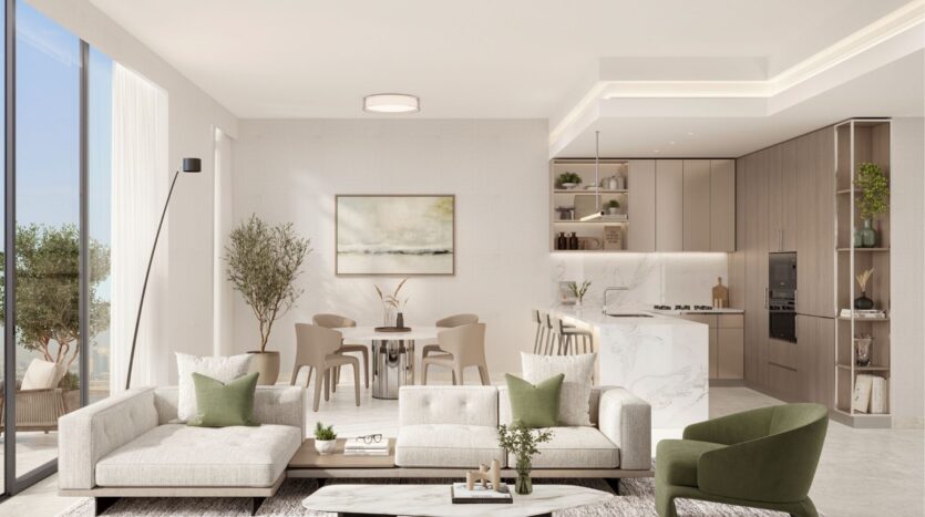 The bright, modern living and dining room at Riverton House by Ellington Properties features neutral tones, two light sofas with green cushions, a marble coffee table, a dining set, plants, large windows, abstract wall art and a sleek kitchen.