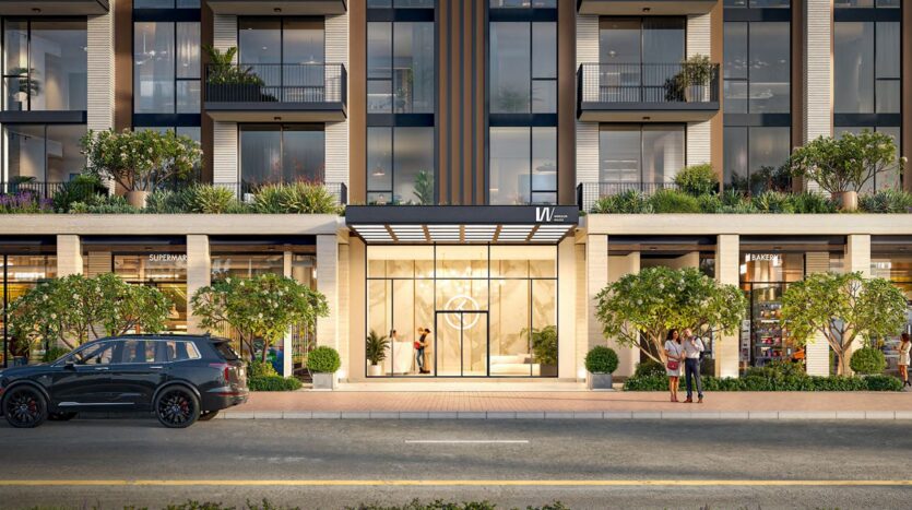 Entrée d'un immeuble moderne, Windsor House de Ellington Properties, avec de grandes portes vitrées, des plantes en pot, des magasins de chaque côté, un SUV noir garé, et des personnes marchant ou se tenant debout près de l'entrée.