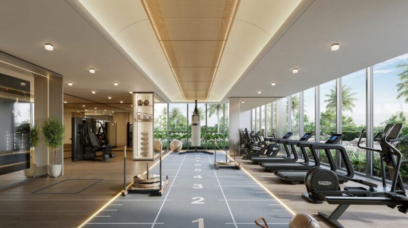 Salle de sport moderne à Windsor House de Ellington Properties avec tapis de course, vélos d'appartement, poids et matériel d'entraînement. De grandes fenêtres laissent apparaître les palmiers et la verdure à l'extérieur, ce qui permet à la lumière naturelle de remplir l'espace d'entraînement spacieux et bien éclairé.