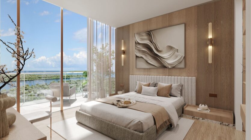 Chambre moderne à wynwood horizon de Imtiaz avec des tons neutres, un grand lit, de l'art mural abstrait, des fenêtres allant du sol au plafond et un balcon offrant des sièges extérieurs et une vue pittoresque sur l'eau et la verdure sous un ciel radieux.