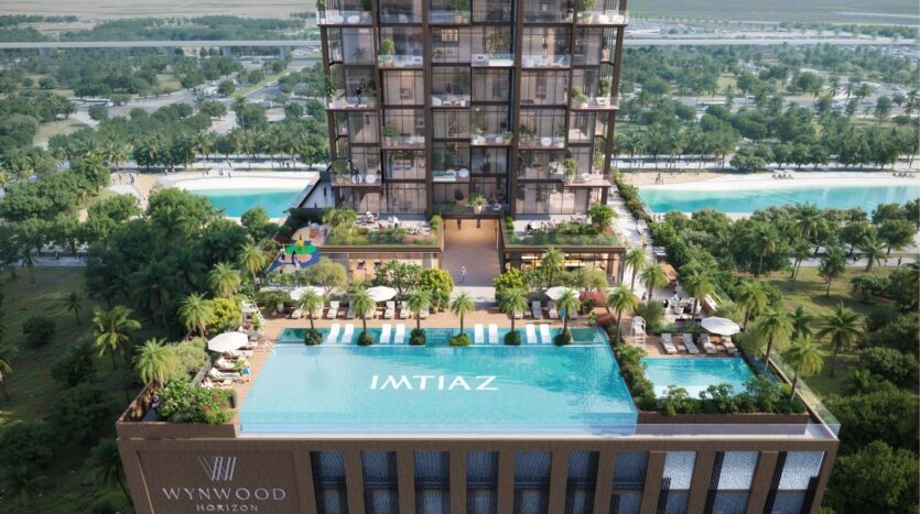 Vue aérienne de la tour moderne Wynwood Horizon de Imtiaz, qui comprend une piscine sur le toit, des espaces de détente, une végétation luxuriante et des balcons. Des palmiers entourent le bâtiment, avec un grand parc et des routes en arrière-plan. La piscine porte l'inscription "IMTIAZ".
