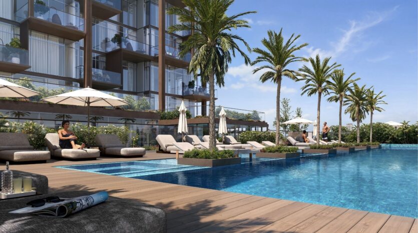 La piscine extérieure moderne du Wynwood Horizon d'Imtiaz comprend des chaises longues, des parasols et des palmiers à côté d'un bâtiment en verre. Les gens se détendent au bord de la piscine sous un ciel bleu ensoleillé, avec une boisson et un magazine sur une table voisine.