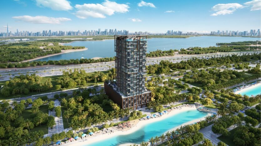 Un grand bâtiment moderne se dresse à l'horizon de wynwood de Imtiaz, entouré d'une verdure luxuriante, d'une route sinueuse et d'une eau turquoise avec des plages de sable, le tout sur fond d'horizon de ville lointaine sous un ciel bleu avec des nuages épars.