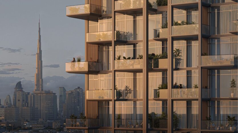 Immeuble d'appartements moderne avec balcons en verre et plantes en pot au premier plan ; à l'arrière-plan, la ligne d'horizon de la ville avec le Burj Khalifa au coucher du soleil, capturant parfaitement l'allure vibrante de l'horizon de Wynwood de Imtiaz.