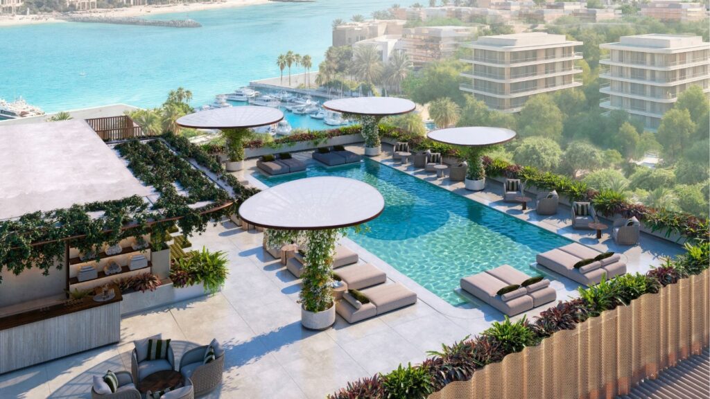 The rooftop pool, equipped with sun loungers, large round umbrellas and greenery, overlooks a marina with yachts, turquoise water and modern buildings like Avida Residences Dubai Islands, surrounded by trees.