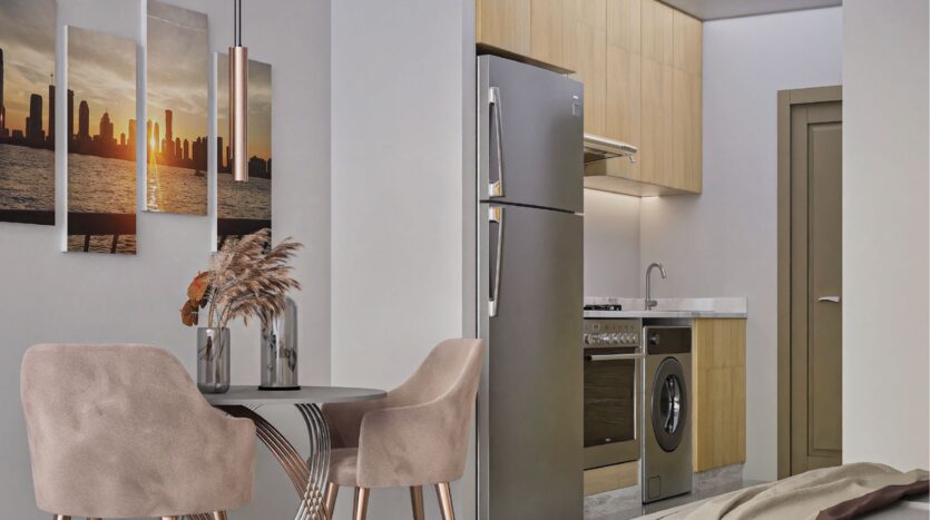 A modern kitchen with light wood cabinets, stainless steel appliances and a round dining table with two pink chairs offers Butterfly Towers Arjan-inspired style. A wall painting of a city sunset and dried flowers complete the ensemble.