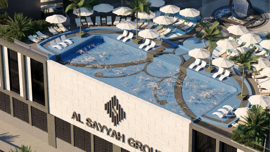 The rooftop pool at Butterfly Towers Arjan features sun loungers, parasols, palm trees and the inscription "AL SAYYAH GROUP" on the building's exterior wall. The modern design includes two interconnected swimming pools and numerous relaxation areas.