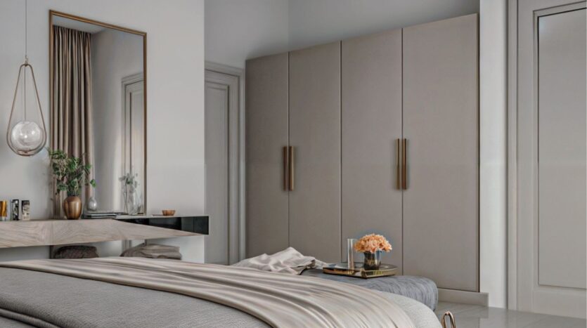 Neutral-toned modern bedroom in Butterfly Towers Arjan, featuring a king-size bed, floating desk with mirror above, pendant lamp, beige cabinets with long handles, and a small tray with flowers on the bed.