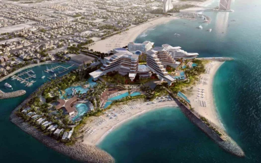 Vista aérea de un moderno complejo turístico en una isla artificial de Dubai, con piscinas, playas de arena, palmeras y aguas circundantes cerca de la costa y los puertos deportivos de la ciudad, con edificios, carreteras y un casino MGM al fondo.