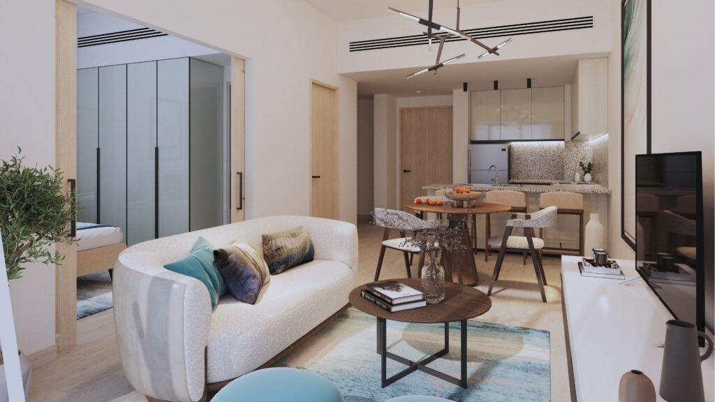 Moderno salón y cocina de planta abierta en el distrito Damac de Dubai, con un sofá blanco, cojines de colores, mesa de centro redonda de madera, mesa de comedor, decoración minimalista y un dormitorio con un armario de cristal visible a través de una puerta corredera.