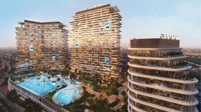 Un moderno complejo de edificios altos con singulares balcones escalonados y una gran piscina central rodeada de palmeras. Situados en el distrito Damac de Dubai, los edificios llevan el logotipo "DAMAC" y tienen vistas a un paisaje urbano al atardecer.