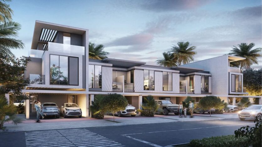 The modern two-storey townhouses on Damac Islands 2 feature large bay windows, carports with several parked cars, palm trees and people standing outside, all under partly cloudy evening skies.