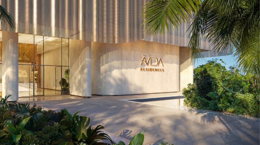 Entrance to the modern Avida Residences Dubai Islands, with large glass doors, beige walls, lush tropical plants and sunlight streaming through the palm trees.