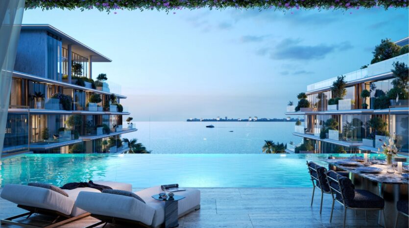Les appartements de luxe modernes avec balcon en verre donnent sur une piscine à débordement au coucher du soleil sur les îles Silena de Dubaï. Des chaises longues et une élégante table à manger sont disposées au bord de la piscine, tandis que les yachts et la silhouette de la ville scintillent au loin.