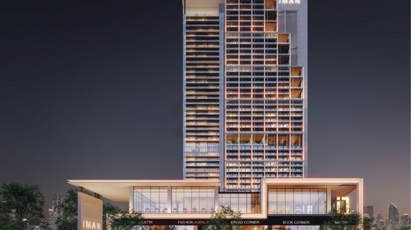 Immeuble moderne de nuit avec des fenêtres éclairées ; la partie inférieure comporte des espaces commerciaux étiquetés "LATTE", "FASHION AVENUE", "BREAD CORNER" et "BOOK CORNER". Le bâtiment est marqué "IMAN" et appartient à Sierra by IMAN.