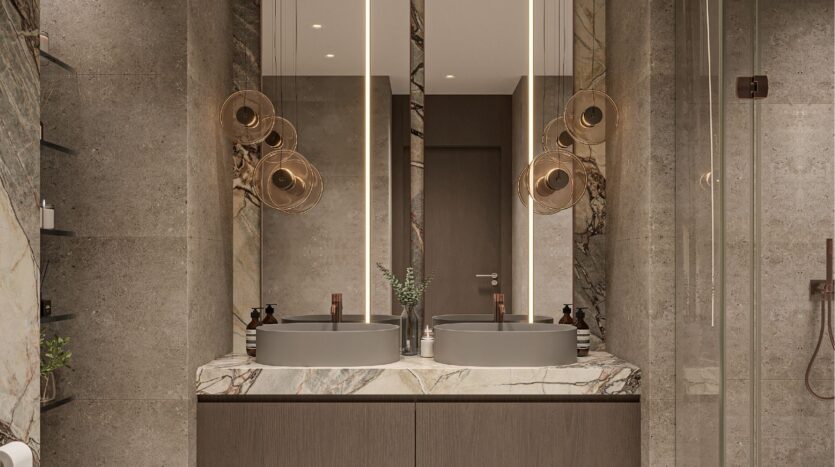 Salle de bains moderne avec double lavabo, comptoir en marbre et grands miroirs éclairés. Des lampes suspendues de la collection Sierra by Iman sont suspendues au-dessus des lavabos, complétant les portes de douche en verre et le design épuré et contemporain dans des tons neutres.
