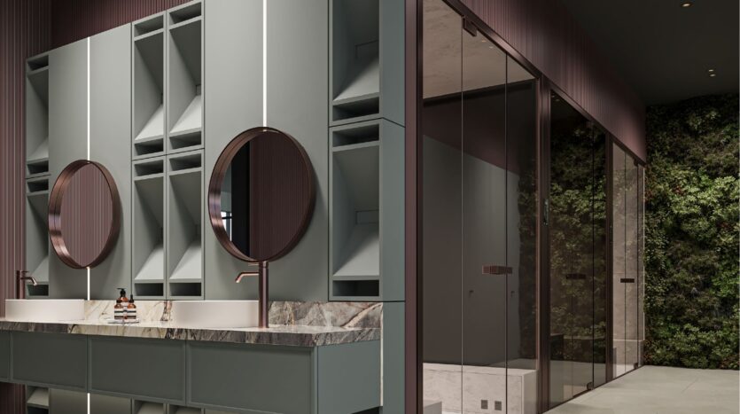 Salle de bains moderne avec deux miroirs ronds au-dessus d'un comptoir en marbre, des armoires gris clair, des luminaires or rose et une douche en verre. Un jardin vertical vert décore le mur à l'extérieur de la douche, avec des touches inspirées de Sierra by Iman.