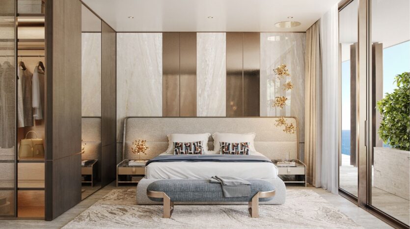 Chambre à coucher moderne au Silena Dubai Islands avec un grand lit, des oreillers à motifs, une banquette élégante et des accents dorés. Les portes vitrées s'ouvrent sur un balcon avec une plante verte et une vue sur l'océan. Un placard avec des portes en verre est visible sur la gauche. Espace lumineux et minimaliste.