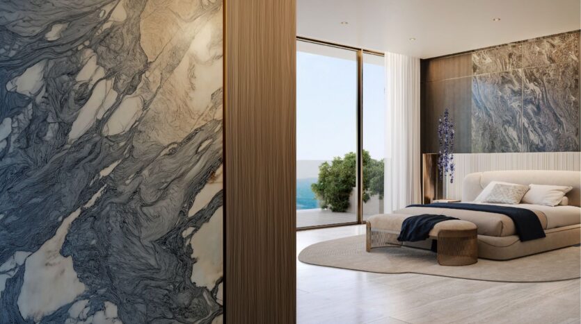 La chambre à coucher moderne et élégante de l'hôtel Silena Dubai Islands est dotée de murs en marbre, d'un grand lit, d'un ottoman rond, de fenêtres allant du sol au plafond et d'une vue sur l'océan et la verdure luxuriante. Des tons neutres et un éclairage doux créent une atmosphère sereine.