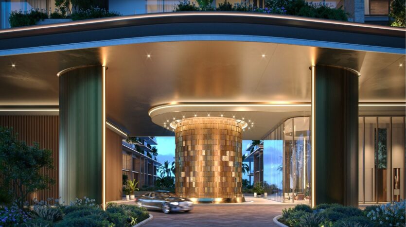 L'entrée d'un hôtel de luxe aux îles Silena de Dubaï présente un auvent moderne et élégant avec des lumières et une structure centrale cylindrique dorée. Une voiture s'approche de l'entrée, entourée de verdure et de bâtiments contemporains.