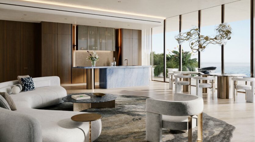 Le salon et la salle à manger modernes de l'hôtel Silena Dubai Islands sont décorés d'un mobilier clair et neutre, d'un îlot de cuisine en marbre bleu, de grandes fenêtres offrant une vue sur l'océan et d'œuvres d'art contemporaines. La lumière naturelle remplit cet espace élégant et minimaliste.