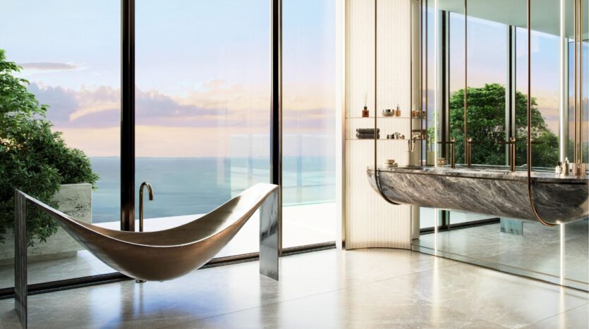 Salle de bains moderne à Silena Dubai Islands avec une baignoire métallique sculpturale, un lavabo en marbre et des fenêtres allant du sol au plafond donnant sur l'océan et la verdure luxuriante, le tout baigné dans la lumière naturelle du coucher de soleil.