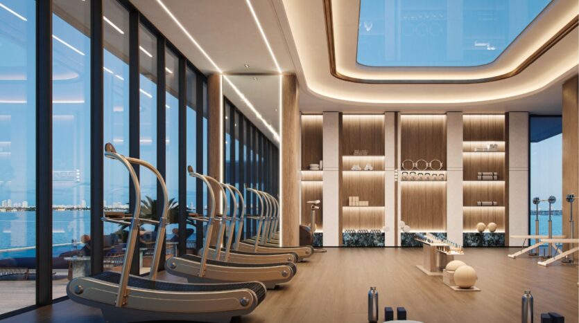 La salle de sport moderne de l'hôtel Silena Dubai Islands est dotée de grandes fenêtres donnant sur le front de mer. Elle comprend des tapis de course, des poids libres, des tapis de yoga et des équipements de remise en forme bien rangés dans un intérieur spacieux et bien éclairé avec des accents en bois.