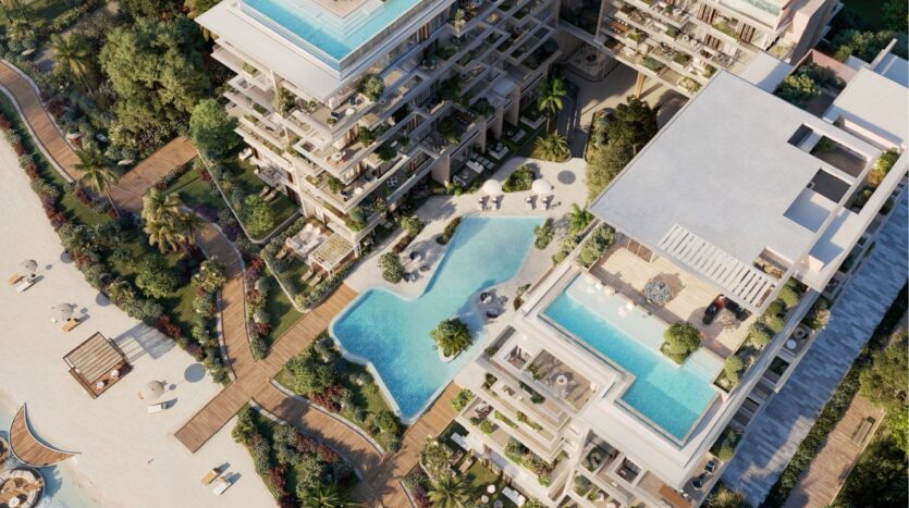 Vue aérienne de la station balnéaire Silena Dubai Islands, qui comprend plusieurs piscines, des espaces de détente, une végétation luxuriante et un accès direct à une plage de sable bordée de parasols et de chaises longues.