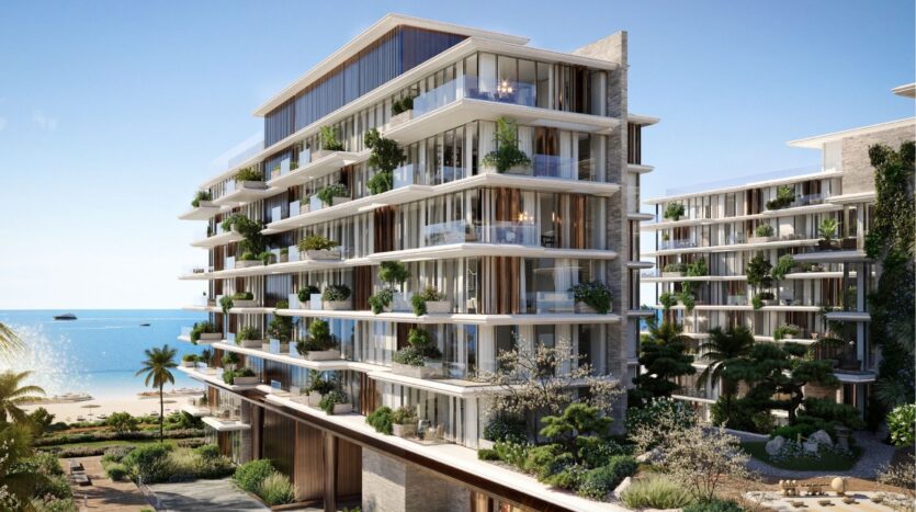 Immeuble moderne d'appartements en bord de mer avec balcons en verre et verdure luxuriante, niché parmi les palmiers sur les îles Silena Dubai, donnant sur une plage de sable et l'océan sous un ciel bleu limpide.