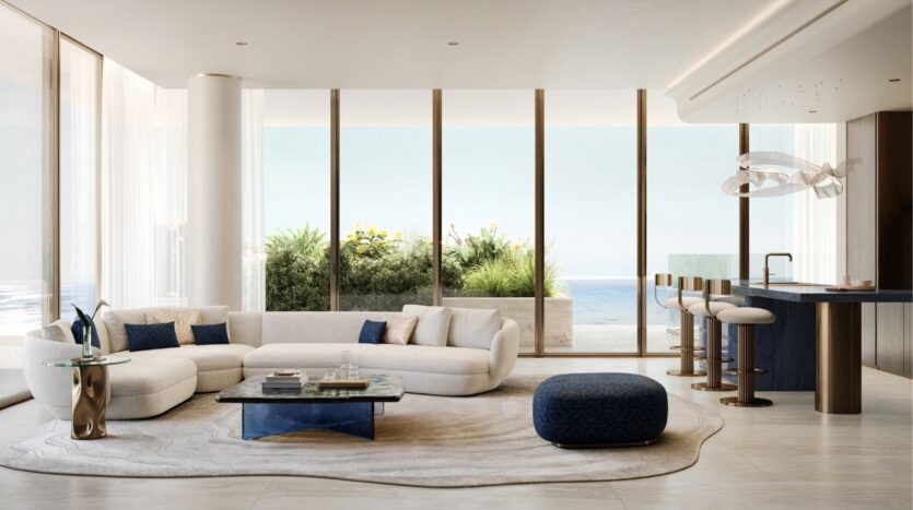 Salon moderne avec de grandes fenêtres donnant sur l'océan à Silena Dubai Islands, comprenant un canapé blanc incurvé, un ottoman bleu, une table basse en marbre, des tabourets de bar, et une cuisine ouverte élégante avec un décor raffiné et la lumière naturelle.