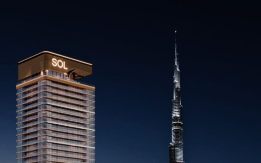 A modern tower, the Sol Luxe Tower, is illuminated at night and stands next to the taller, needle-like Burj Khalifa against a dark sky.