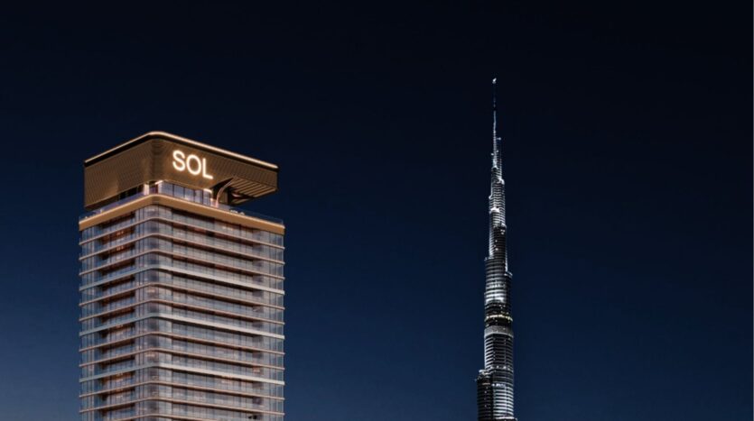 Una torre moderna, la Sol Luxe Tower, è illuminata di notte e si erge accanto al Burj Khalifa, più alto e simile a un ago, in un cielo scuro.
