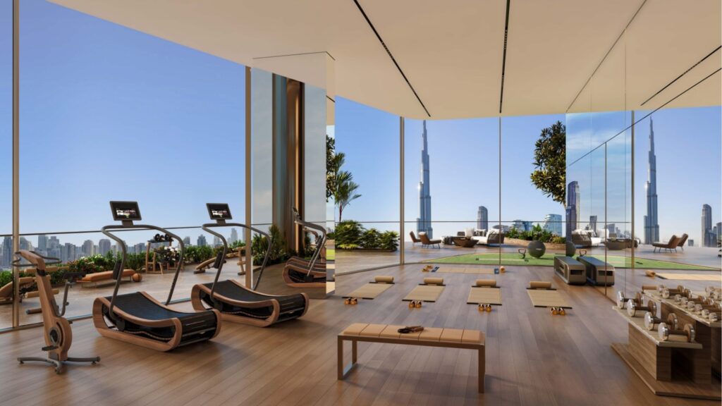 Moderna palestra con pavimenti in legno, tapis roulant, tappetini per lo yoga e sedie a sdraio, con ampie vetrate e vista panoramica sullo skyline della città dalla torre Sol Luxe, compreso l'iconico Burj Khalifa.
