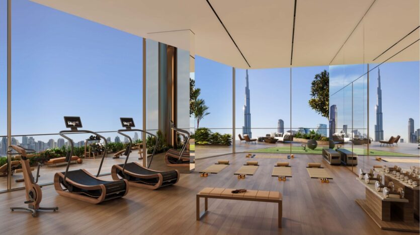 Moderna palestra con pavimenti in legno, tapis roulant, tappetini per lo yoga e sedie a sdraio, con ampie vetrate e vista panoramica sullo skyline della città dalla torre Sol Luxe, compreso l'iconico Burj Khalifa.