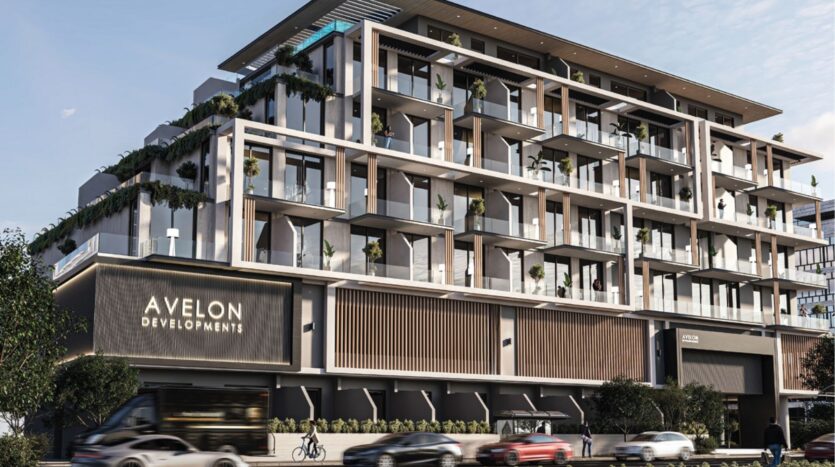 Immeuble d'appartements moderne de plusieurs étages avec de grands balcons, des garde-corps en verre et de la verdure à chaque niveau. L'enseigne indique "Avelon Developments". Des voitures et un bus passent devant l'immeuble.