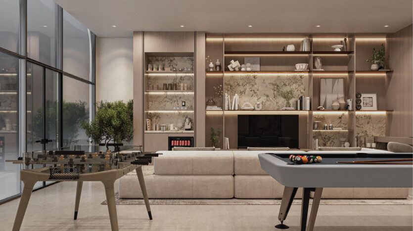 Salon moderne avec des murs en verre, un baby-foot et un billard au premier plan. Des étagères contenant de la décoration et des livres entourent une cheminée en marbre derrière un grand canapé sectionnel beige. Éclairage d'ambiance chaleureux dans tout le salon.