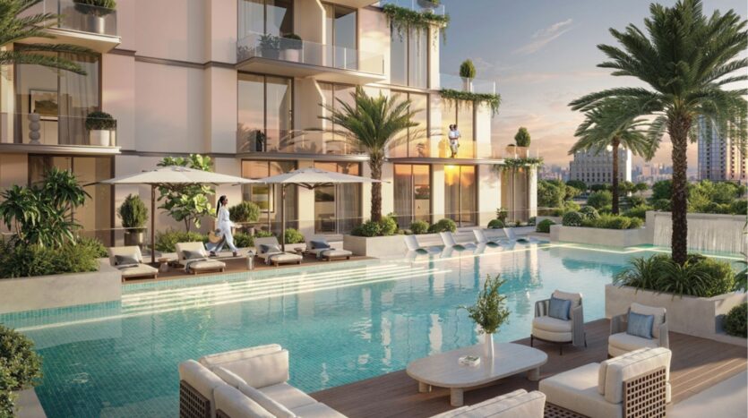 Ce complexe d'appartements modernes avec balcons donne sur une luxueuse piscine extérieure entourée de chaises longues, de parasols, de palmiers et de verdure. Au coucher du soleil, des personnes se détendent près de l'eau et s'assoient.