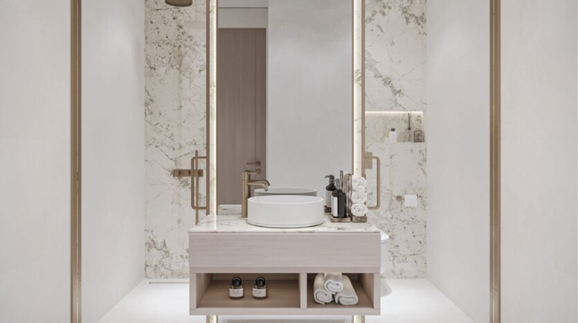 Une salle de bains moderne et minimaliste avec un lavabo en marbre blanc, un évier rond, des articles de toilette, des serviettes pliées et des murs en marbre avec des étagères encastrées. L'espace est lumineux et épuré, avec des tons neutres.