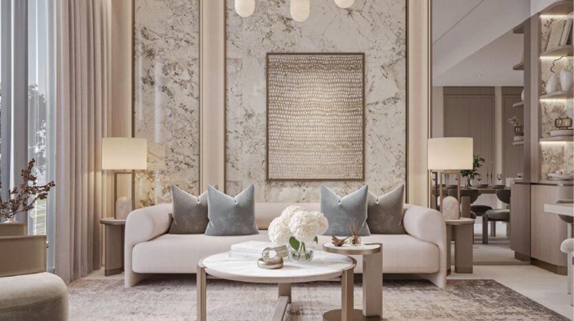 Salon moderne avec un canapé beige clair, des coussins gris, un mur d'accent en marbre, une table basse ronde avec des fleurs et un décor aux tons neutres. L'éclairage chaleureux des lampes de table et les grandes fenêtres illuminent l'espace.